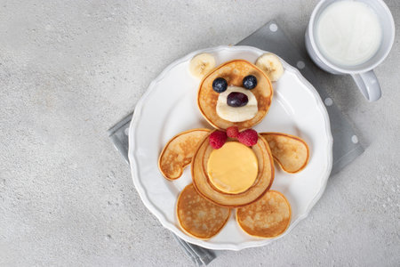Fun idea for kids breakfast - bear-shaped pancakes with blueberries, raspberries, banana and cup of milkの写真素材