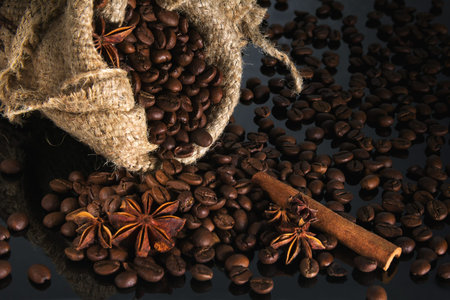 coffee grains into the sack and scattered on a black background with an anise and cinnamon