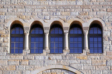 five old windows with arches, columns and lattices on a stone brown wall