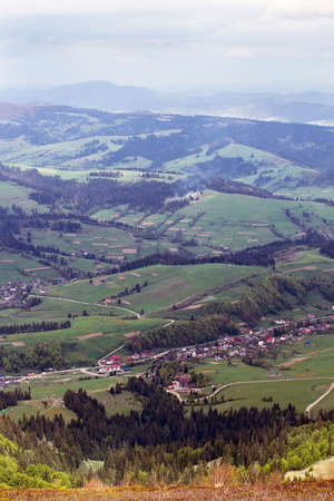landscape consisting of a Carpathians mountains with green trees and fir-tree and grassy valley with little house and blue sky with white cloudsの写真素材