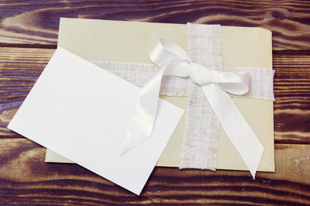 envelope with white ribbon and white blank card on a wooden backgroundの写真素材