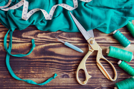 A collection of sewing tools and green fabric with threads on a wooden brown background