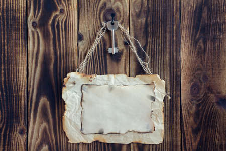 key hanging on a nail and scorched paper hanging on a rope on a wooden brown backgroundの写真素材