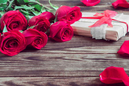gift and red roses with petal on a wooden brown backgroundの写真素材