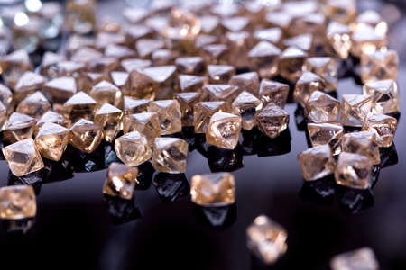 Collection of faceted natural transparent diamonds in macro with yellow reflection in the black backgroundの写真素材