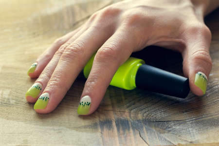 green nail polish and skin care of a beauty female hands with green and white moon nail art manicure on a wooden backgroundの写真素材