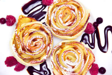 three apple muffins with raspberries and  blueberries, drizzled with chocolate sauce leaving a zigzag trail on a white plateの写真素材