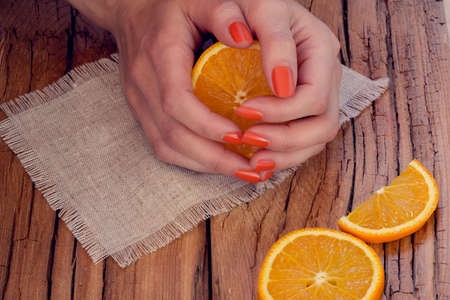sliced oranges and skin care of a beauty female hands with orange manicure on a sackcloth and wooden backgroundの写真素材