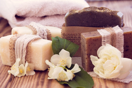 Decorated pieces of various dry soap with a jasmine, a rose and towel on a wooden background