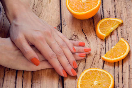 sliced oranges and skin care of a beauty female hands with orange manicure on a wooden backgroundの写真素材
