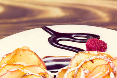 two apple muffins with raspberry drizzled with chocolate sauce leaving a zigzag trail on a white plate on a wooden backgroundの写真素材