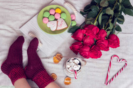 womens legs in a socks and breakfast in bed with red roses, sweater and heart of sugar candies and cup of coffee, marshmallow, macaroon and gingerbread cookie on a salver. Still life for St. Valentine's Dayの写真素材