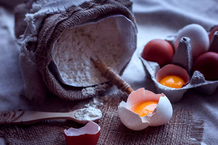 flour with spoon in a sack and broken eggsの写真素材
