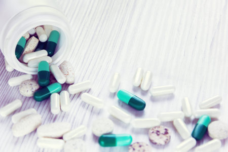 different pills are getting out of the bottle on a white wooden backgroun