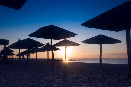 silhouette of straw umbrellas on the sea coast at sunriseの写真素材