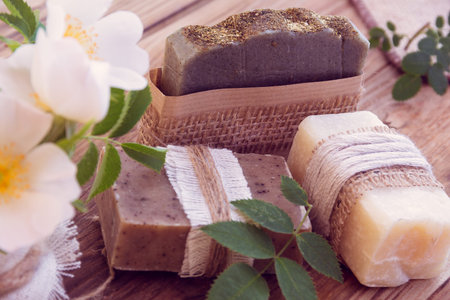 Three pieces of dry soap with white roses on a wooden background