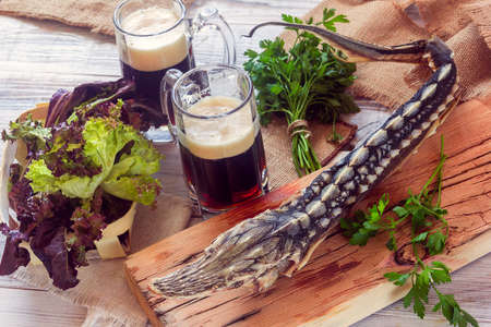 dried sturgeon with dark beer and greens on a wooden backgroundの写真素材
