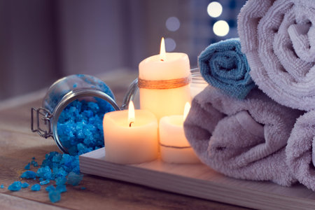 SPA consist from towels, blue sea salt and candle on a wooden background with backlight