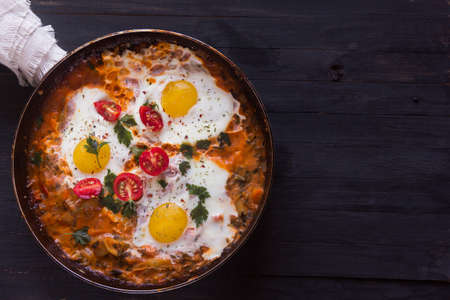 three fried eggs with Ñherry tomatoes in a pan on a black background with spaceの写真素材