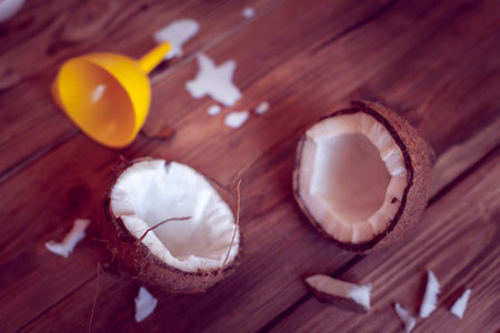 two half of coconut with yellow funnel and spilled milk on a wooden background