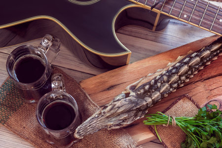 dried sturgeon with dark beer, greens and  guitar on a wooden background