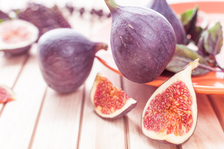 Sliced figs in an orange bowl on a wooden striped background