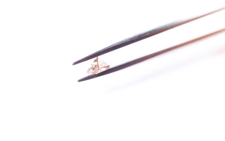 natural transparent diamond in the form of a pyramid in tweezers in macro