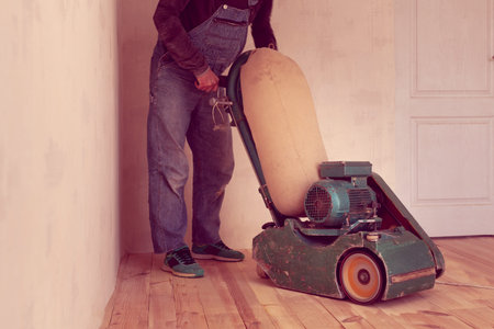 carpenter polishes a wooden floor by electric grinding wood machine in a room