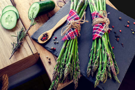 bunches of asparagus with spices and cucumber on a black boardの写真素材