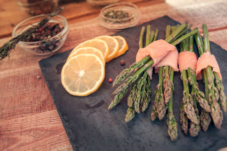 bunches of asparagus wrapped in salmon with spices on a black boardの写真素材