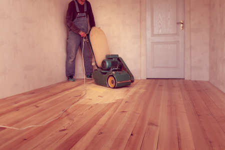 carpenter polishes a wooden floor by electric grinding wood machine in a roomの写真素材