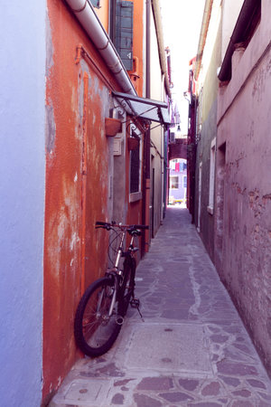 narrow street on a burano island with orange house and bicycle