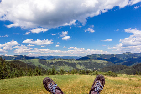 landscape consisting of a Carpathians mountains with legs sticking out and green grassy valley in the foreground  and cloudy sky on the backgroundの写真素材