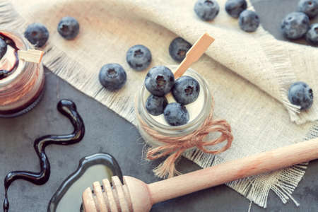 two jars of yogurt with blueberries, honey and chocolateの写真素材