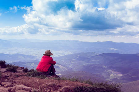 the tourist sits at mountain top against the background of majestic mountainsの写真素材