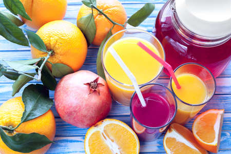 freshly squeezed orange and pomegranate juices with oranges and pomegranate fruit on a blue wooden backgroundの写真素材