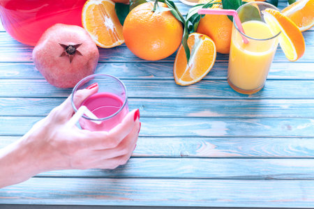 freshly squeezed pomegranate juice in a women's hand with oranges and pomegranate fruit on a blue wooden backgroundの写真素材