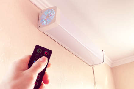 hand from remote-controlled includes bactericidal air recirculator hanging on wall for quartzing air in roomの写真素材