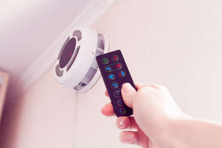 female hand by remote control turning on ventilation system as a recuperator for fresh indoor air qualityの写真素材