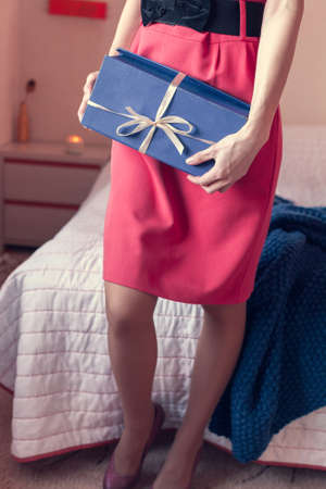 girl in a red dress hold a gift in her hands, standing near the bedの写真素材