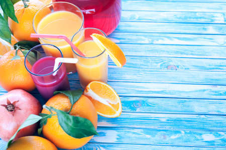 freshly squeezed orange and pomegranate juices with oranges and pomegranate fruit on a blue wooden backgroundの写真素材