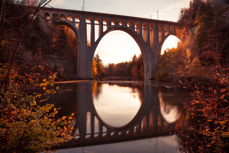 Bridge Reflecting in River at Sunset with Autumn Foliageの写真素材
