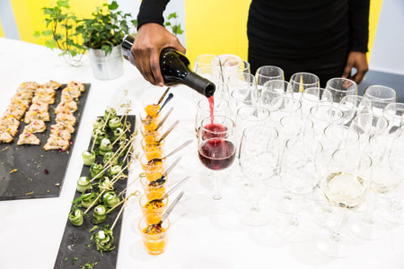 Waitress Pouring Red Wine in Glasses at Buffet Table with White Cloth