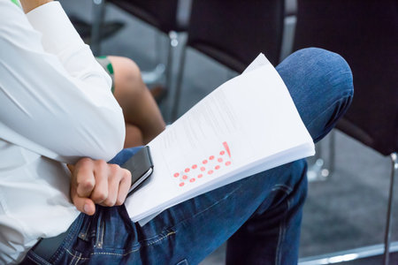 Man Sitting at Conference Meeting with Information Booklet and Mobile Phone on his Lap