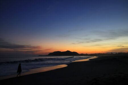 Woman Walking on a Pacific Ocean Sandy Beach at Duskの写真素材