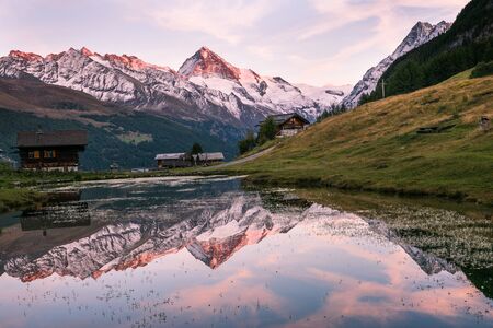 Sunset over Snowy Mountains and Wood Chalet Reflecting in Altitude Lakeの写真素材