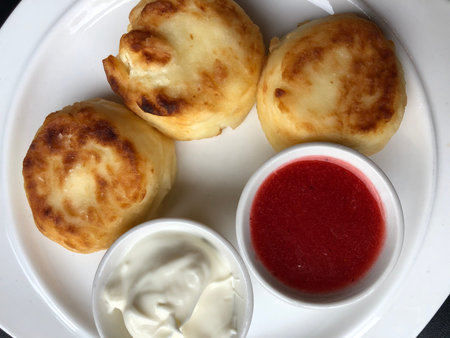 Cottage cheese pancakes with sour cream and strawberry jam on a white plateの写真素材