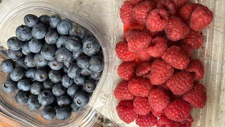 Blueberries and raspberries in plastic containers. Top view.