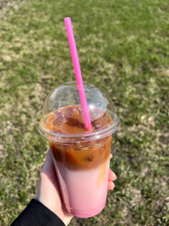 Iced coffee in a plastic cup in hand on green grass backgroundの写真素材