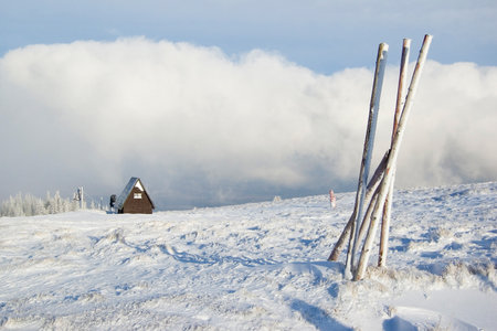 Winter scenery in the mountains with a wooden house covered with snow and clouds in the backgroundの写真素材